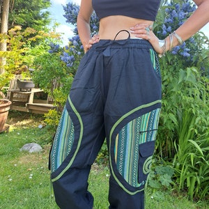 May include: Black pants with green and yellow patterned fabric accents. The pants have a drawstring waist and a relaxed fit.