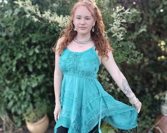 May include: A woman wearing a teal blue, embroidered, asymmetrical dress with a lace trim. She is wearing black leggings and has red hair.