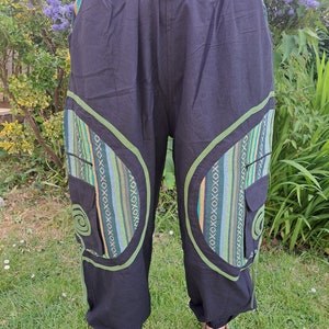 May include: Black pants with green and blue patterned trim and pockets. The pants have a drawstring waist and a relaxed fit.
