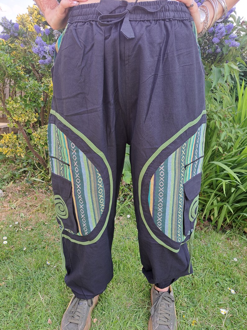 May include: Black pants with green and blue patterned trim and pockets. The pants have a drawstring waist and a relaxed fit.