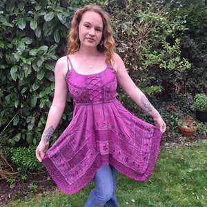Puede incluir: Un vestido morado sin mangas, de corte asimétrico, con ribete de encaje y bordado floral. El vestido tiene un detalle de encaje en la parte delantera y un corpiño ajustado.