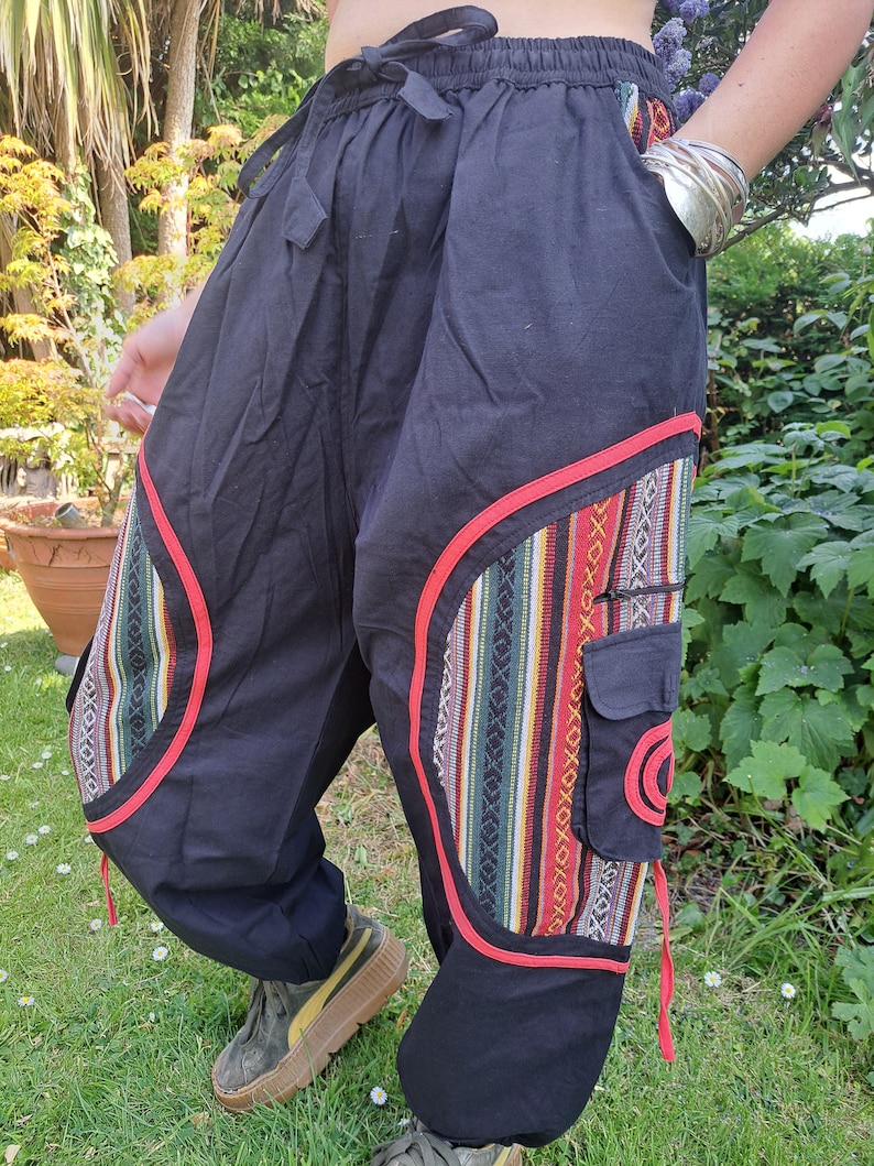 May include: Black pants with red trim and colorful patterned fabric accents. The pants have a drawstring waist and a cargo pocket.