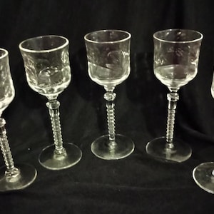May include: Set of five clear glass stemmed wine glasses with a decorative etched pattern. The glasses have a twisted stem.