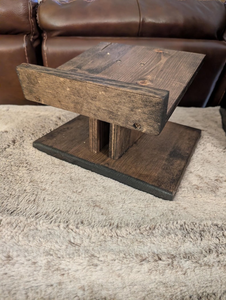 Op de afbeelding: Een donkerbruin gebeitste houten standaard met een rechthoekige voet, een centrale verticale steun en een schuin geplaatst bovenplatform met een opstaande rand aan de voorzijde. De houtnerf is zichtbaar over de gehele constructie met schroeven.