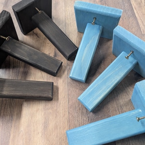 K&ouml;nnte beinhalten: Vier Holz-Regalbretter, zwei in Dunkelbraun und zwei in Hellblau lackiert. Die Halterungen sind abgewinkelt und haben eine Schraube oben.