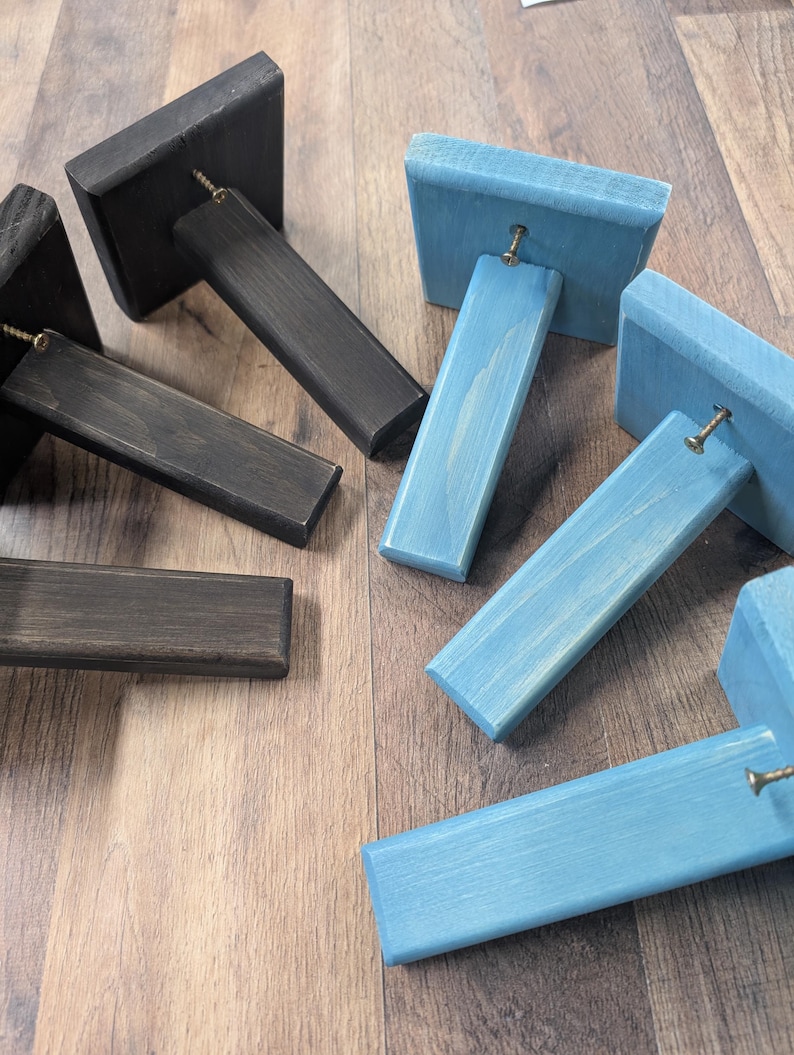 K&ouml;nnte beinhalten: Vier Holz-Regalbretter, zwei in Dunkelbraun und zwei in Hellblau lackiert. Die Halterungen sind abgewinkelt und haben eine Schraube oben.