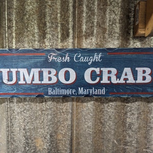 May include: A blue wooden sign with red trim and white lettering that reads "Fresh Caught Jumbo Crabs Baltimore, Maryland".