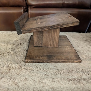 Op de afbeelding: Een donkerbruin gebeitste houten displaystandaard met een platte vierkante voet, een centrale verticale steunpilaar en een schuin geplaatst bovenplatform met een kleine opstaande rand aan de achterkant om voorwerpen stevig vast te houden.