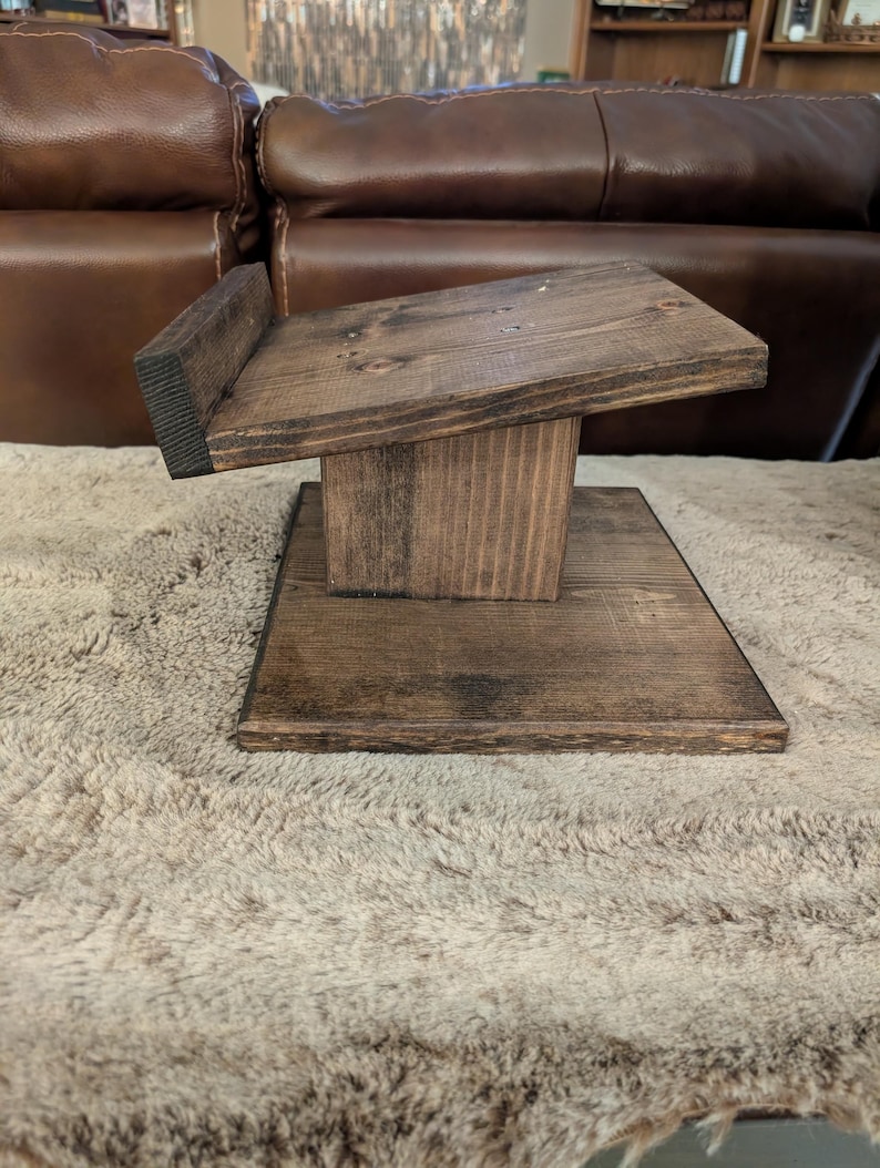 Op de afbeelding: Een donkerbruin gebeitste houten displaystandaard met een platte vierkante voet, een centrale verticale steunpilaar en een schuin geplaatst bovenplatform met een kleine opstaande rand aan de achterkant om voorwerpen stevig vast te houden.