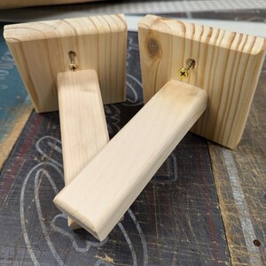 K&ouml;nnte beinhalten: Zwei unfertige Holzregalb&ouml;cke mit befestigten Schrauben. Die B&ouml;cke sind aus hellem Holz und haben eine quadratische Form.