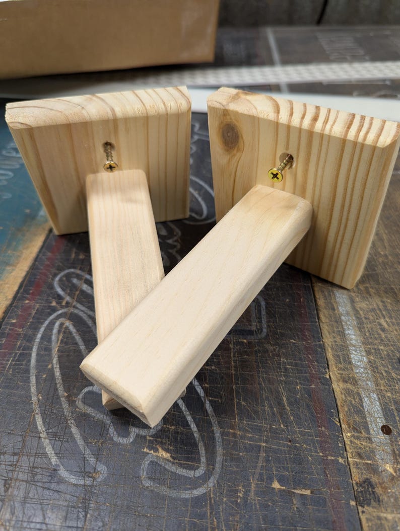 K&ouml;nnte beinhalten: Zwei unfertige Holzregalb&ouml;cke mit befestigten Schrauben. Die B&ouml;cke sind aus hellem Holz und haben eine quadratische Form.