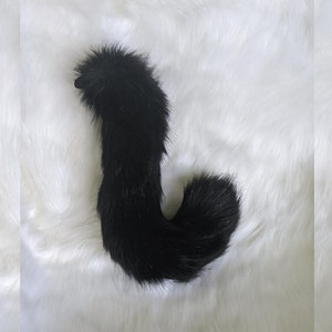 May include: A black fluffy tail with a long, curled tip. The tail is made of faux fur and is designed to be worn as a costume accessory.