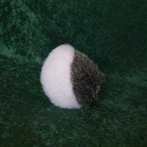 May include: A white and gray fluffy pom pom ball with a long, gray fur tail.