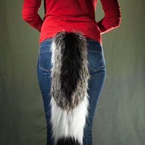 May include: A black, white, and gray faux fur wolf tail worn by a model.