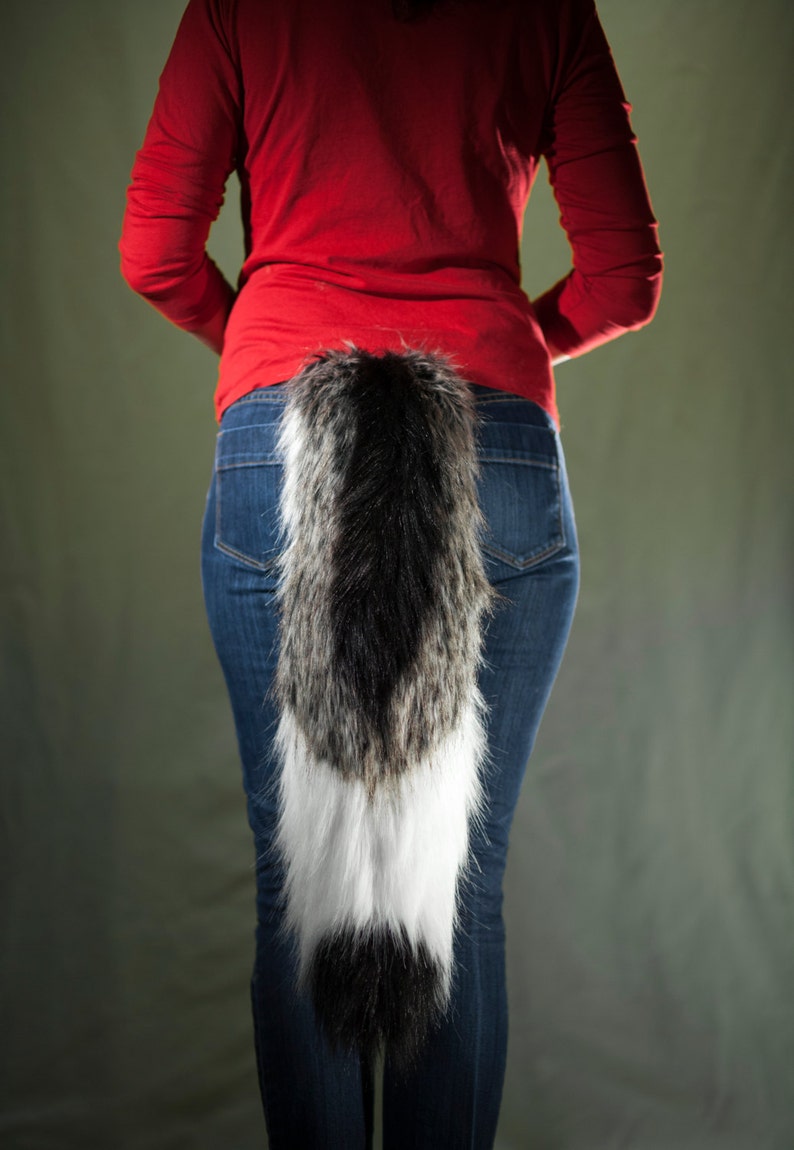 May include: A black, white, and gray faux fur wolf tail worn by a model.