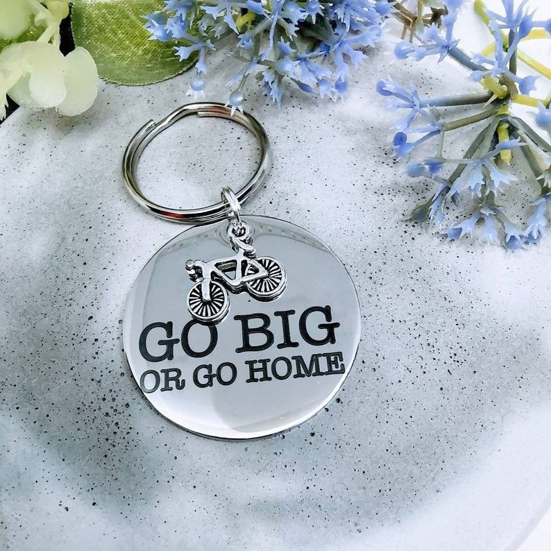May include: Silver keychain with a round metal tag that says "Go Big or Go Home" with a small silver bicycle charm attached.