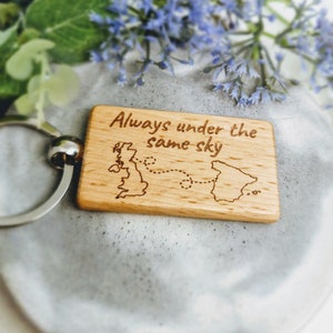 May include: Wooden keyring with a map of the UK and Spain, connected by a dotted line. The text "Always under the same sky" is engraved on the keyring.