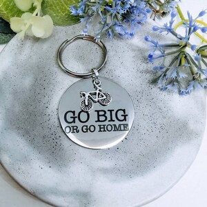 May include: A silver keychain with a bicycle charm and the text "GO BIG OR GO HOME".