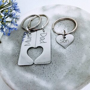 May include: Two silver keychains with interlocking heart cutouts. One keychain says "Dad" and the other says "Mum". A third silver keychain with a heart charm says "Son".