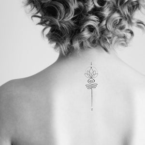 May include: A woman with curly hair has a small, simple line drawing tattoo of a lotus flower on the back of her neck.