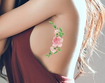 May include: A woman wearing a maroon sleeveless dress with a floral tattoo on her side. The tattoo features pink roses and green leaves.