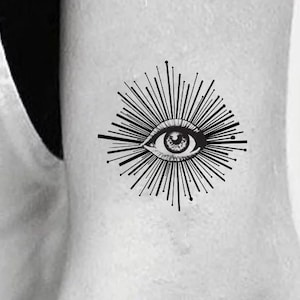 Può includere: Un design di tatuaggio in bianco e nero di un occhio con linee radianti. L'occhio è circondato da un cerchio di linee che irradiano verso l'esterno.