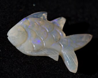 May include: A white opal fish carving with iridescent blue and purple hues. The fish is carved in a realistic style with scales and fins.