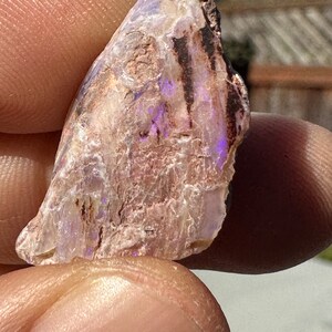 May include: A small, rough, white and purple opal with black veins. The opal is a natural stone with a rough, irregular shape.