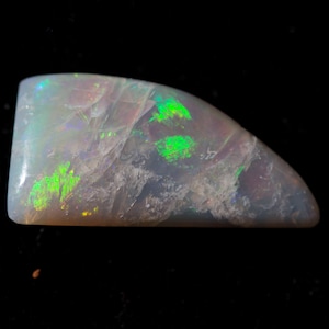 May include: A white opal gemstone with green and blue iridescence. The opal is cut into a teardrop shape and has a smooth, polished surface.