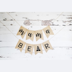 May include: A burlap banner with the words "mama bear" in black lettering. The banner is strung with twine and has a small triangle design in the "bear" section.