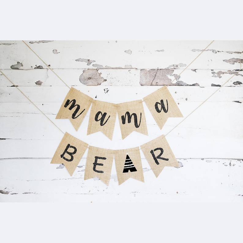 May include: A burlap banner with the words "mama bear" in black lettering. The banner is strung with twine and has a small triangle design in the "bear" section.