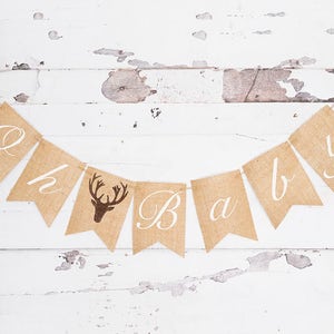 May include: A burlap banner with the words "Oh Baby" in white script. The banner has a brown deer silhouette in the center.