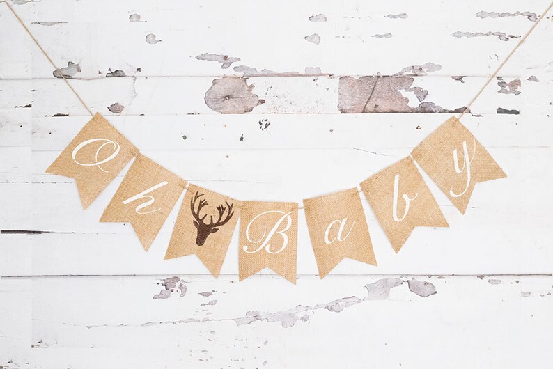 May include: A burlap banner with the words "Oh Baby" in white script. The banner has a brown deer silhouette in the center.
