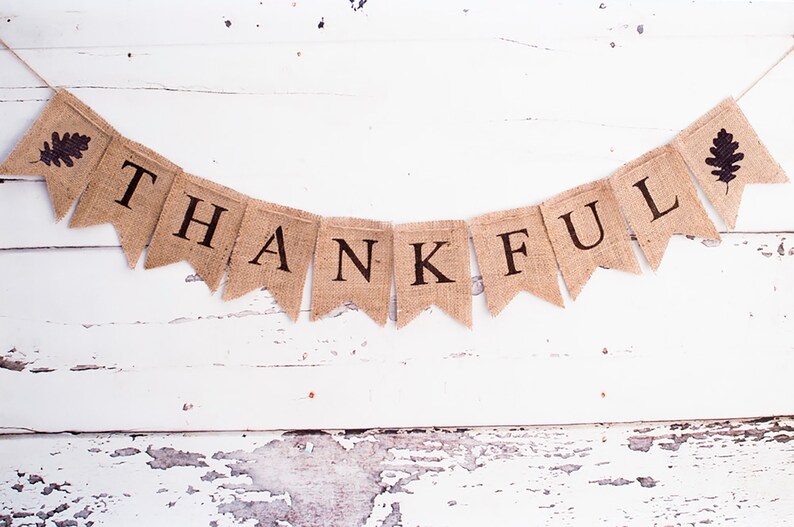 May include: A burlap banner with the word "THANKFUL" printed in black letters. The banner is decorated with two brown leaf shapes on either end.