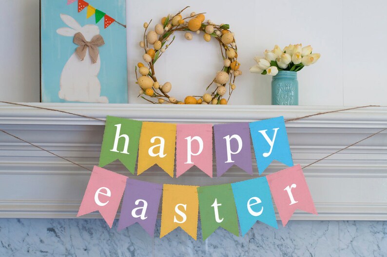May include: A colorful banner with the words "happy easter" hanging on a white mantel. The banner is made of fabric and has a rustic look. There is a wreath with yellow eggs and a vase of white flowers on the mantel.