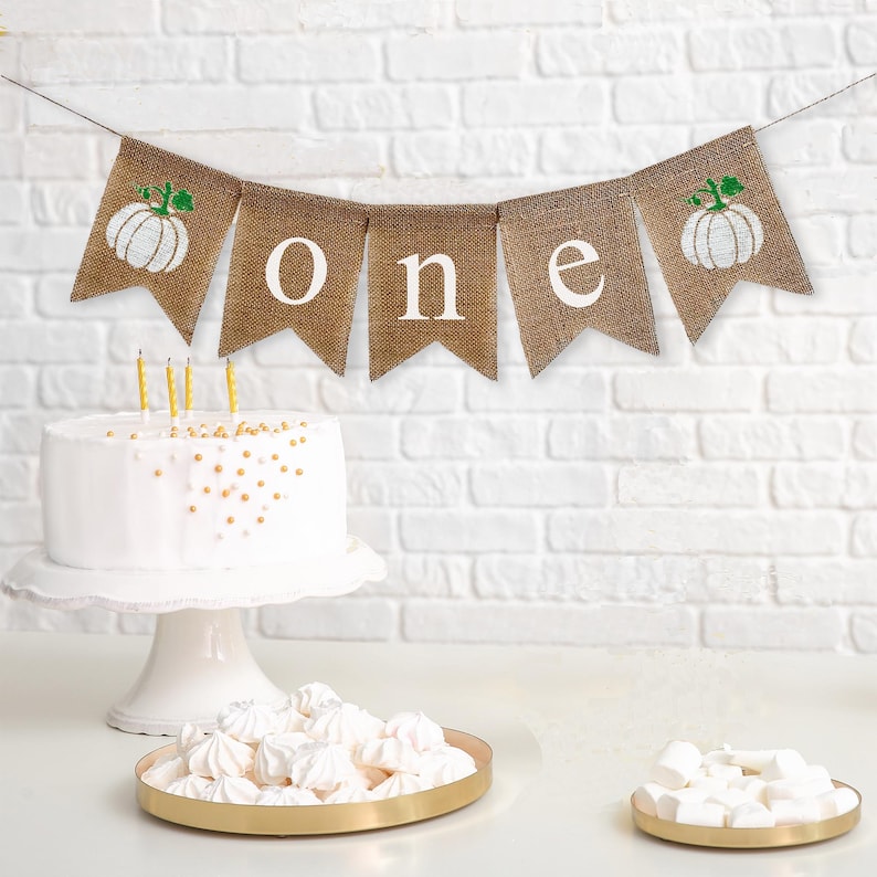 Celebrate one with this white pumpkin burlap banner. With unique white pumpkins on each end and the letters o n e spelled out in between in white lowercase letters, this banner is perfect for a fall first birthday celebration.