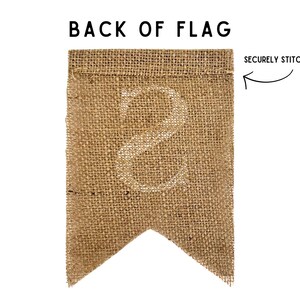 May include: The back of a burlap flag with a white number 8 printed on it. The top edge of the flag is folded over and securely stitched.