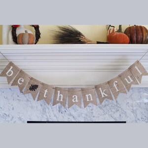 May include: A burlap banner with the words "be thankful" in white lettering. The banner is decorated with a small brown leaf.