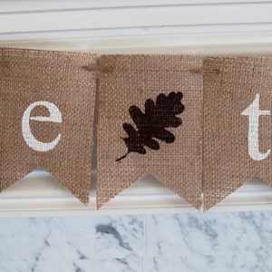 May include: A burlap banner with the word "be" followed by a brown leaf and then the word "t".