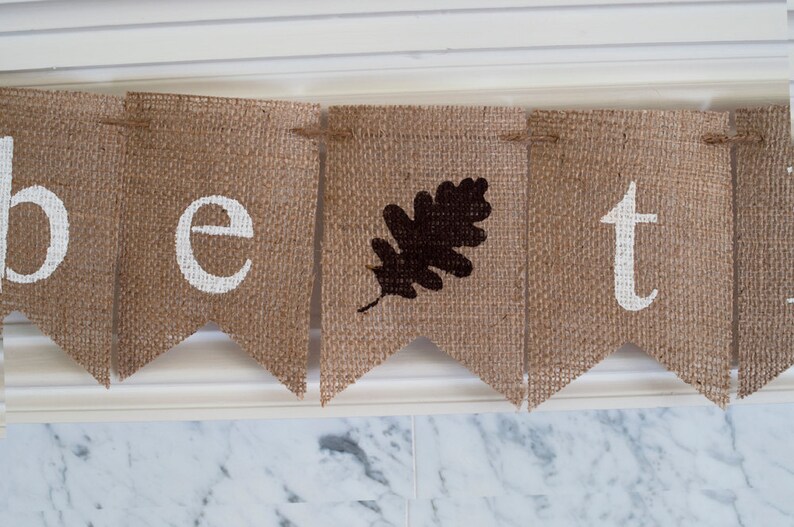 May include: A burlap banner with the word "be" followed by a brown leaf and then the word "t".