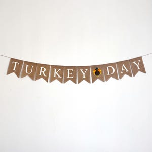 May include: A burlap banner with the words "TURKEY DAY" in white letters. A small turkey illustration is between the words "KEY" and "DAY".