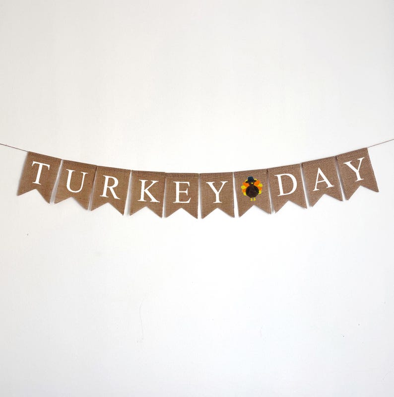 May include: A burlap banner with the words "TURKEY DAY" in white letters. A small turkey illustration is between the words "KEY" and "DAY".