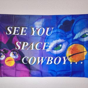 Może przedstawiać: Flaga z podzielonym wzorem w kolorze fioletowym i niebieskim, z białym napisem "SEE YOU SPACE COWBOY...". Flaga przedstawia dwie stylizowane twarze podobne do Furby.