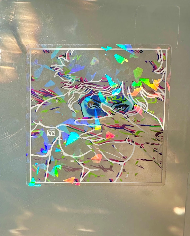 May include: Holographic sticker featuring a stylized illustration of a person with blue eyes and white hair. The artwork is overlaid with iridescent, geometric shapes. The sticker has a clear border and the initials "CYN" are visible.