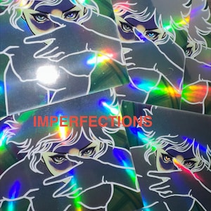May include: Holographic stickers featuring a stylized illustration of a person with blue eyes, partially obscured by their hands. The stickers have a rainbow sheen and the word "IMPERFECTIONS" in red.