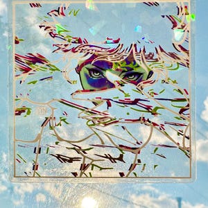 May include: A clear, square sticker featuring an artistic illustration of a person's eyes and part of their face, with a background of abstract lines in green, red, and white. The sticker has a gold border and the initials "CYN" in the corner.