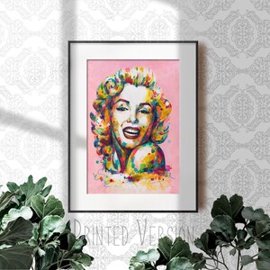 以下が含まれることがあります： マリリン・モンローのカラフルな肖像画の額装されたプリント。肖像画は、明るい色と太い線を使ったポップアートスタイルで描かれています。背景は薄いピンクです。