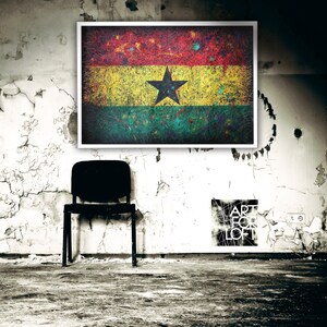 Puede incluir: Una impresi&oacute;n enmarcada de la bandera de Ghana con un aspecto desgastado y texturizado. La bandera es roja, amarilla, verde y negra con una estrella negra de cinco puntas en el centro. La impresi&oacute;n est&aacute; colgada en una pared blanca con pintura descascarada. Una silla negra se encuentra frente a la impresi&oacute;n.