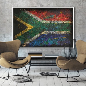 May include: A framed artwork depicting the South African flag, rendered with colorful, scribbled lines. The artwork hangs above a dark console table, flanked by two brown armchairs with black metal frames. A modern living room setting.