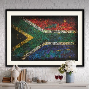 May include: Framed artwork featuring the South African flag, rendered with colorful, textured lines against a black background. The flag's design includes red, white, green, yellow, blue, and black. The artwork is displayed above a white cabinet with decorative items.